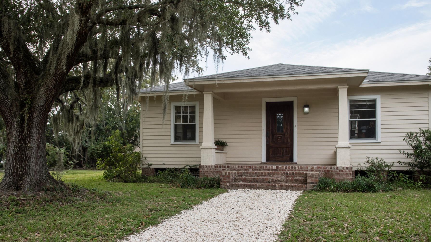 A modest Florida bungalow from the front walk, live oak and morning light.